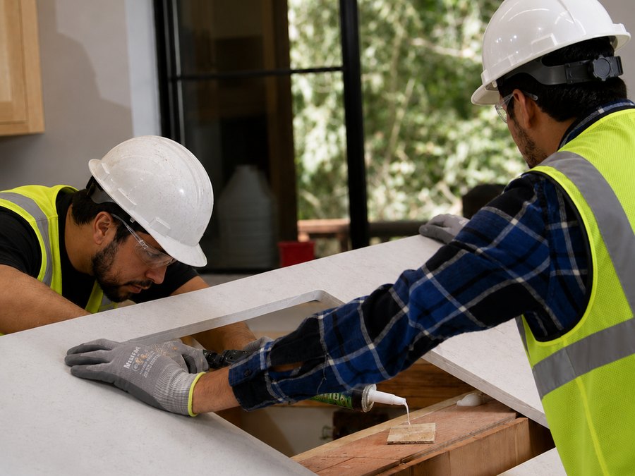 Two-person install crew bedding and sealing a countertop deck at a sink cutout